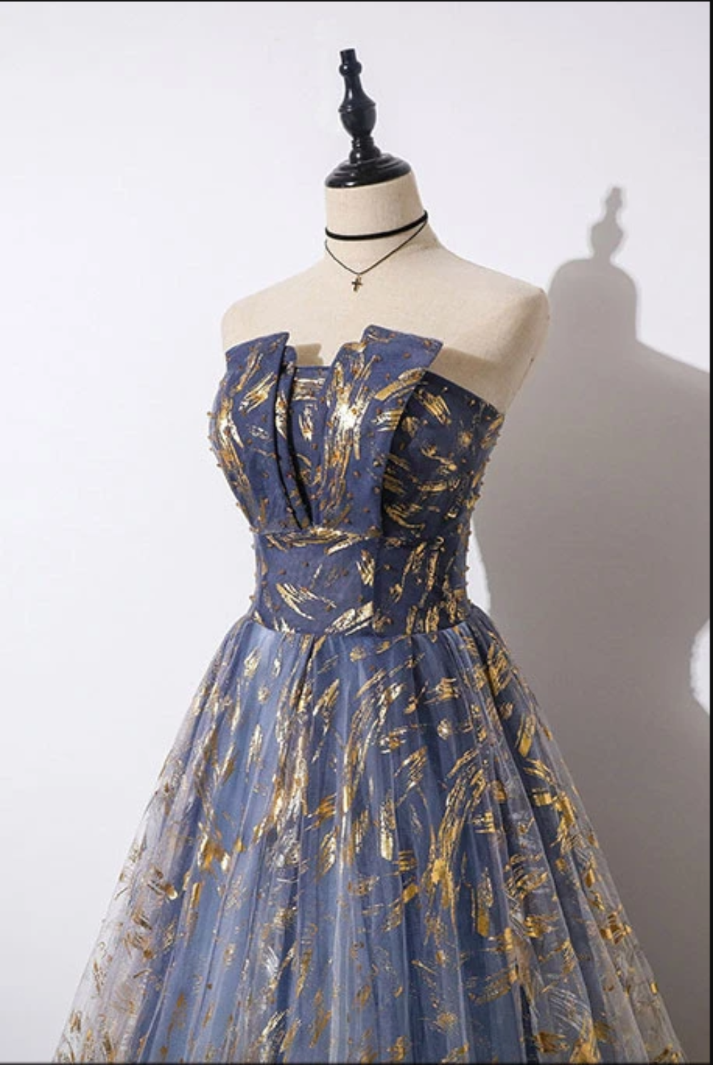 Blue evening gown with gold patterns on a mannequin against a white background