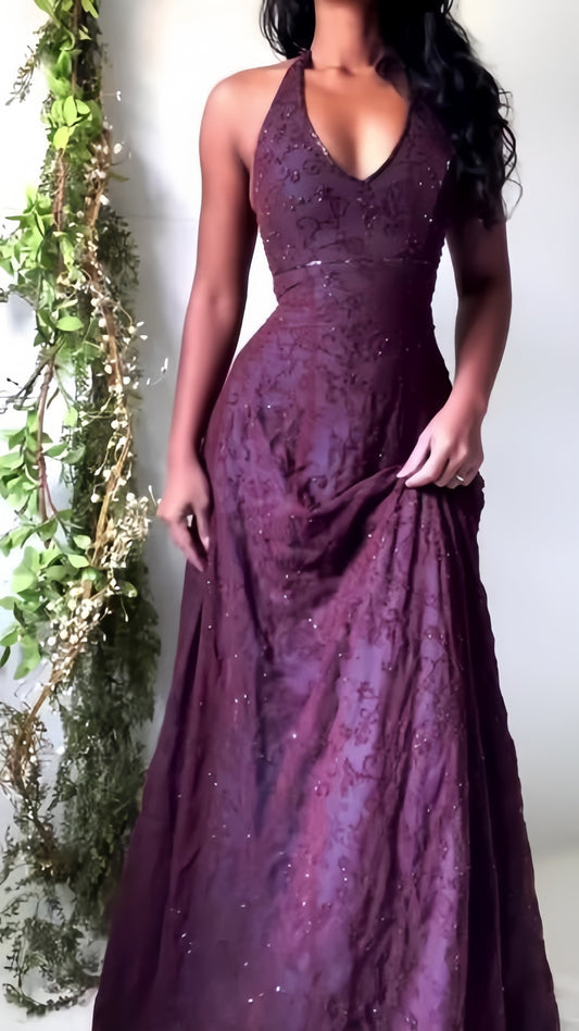 Woman wearing a burgundy evening gown with a halter neckline against a white wall.